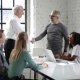 An employer shakes an employees hand at a conference table with other employees.